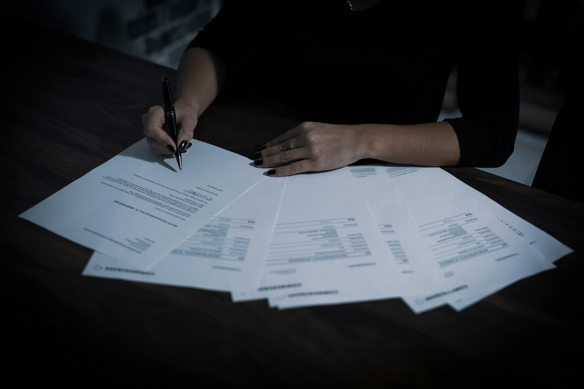 Hands working through documents spread across a table in low light